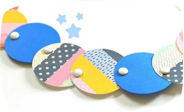 A colorful garland made of overlapping paper circles in blue, yellow, pink, and patterned designs, connected with brad fasteners.